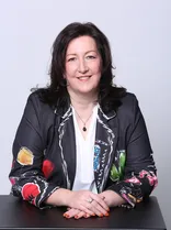 Nicole Falkenstein, Halbportrait, sitzend, lächelnd, Blick in Kamera, neutraler Hintergrund